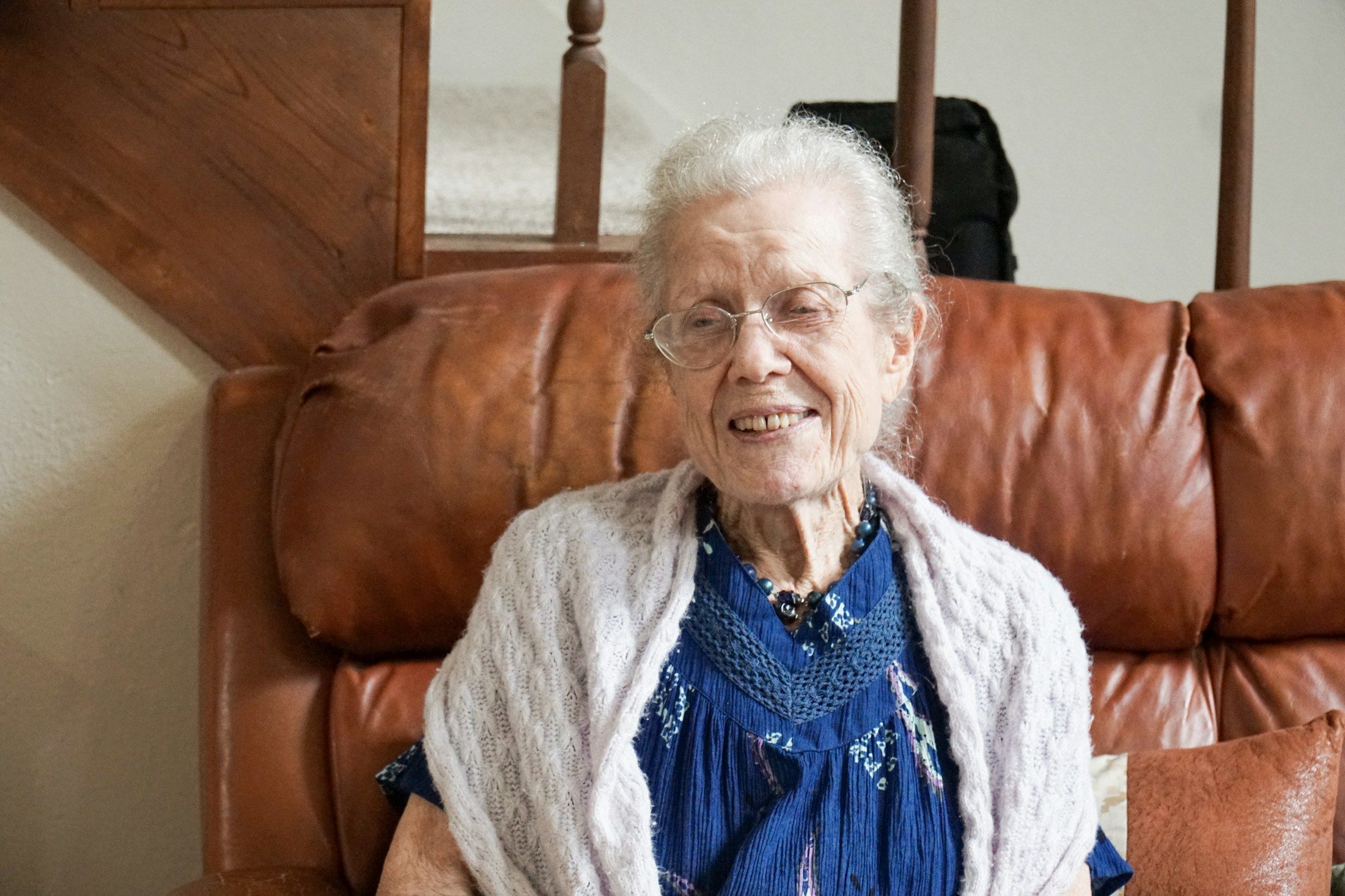 An older woman smiling in a leather armchair.