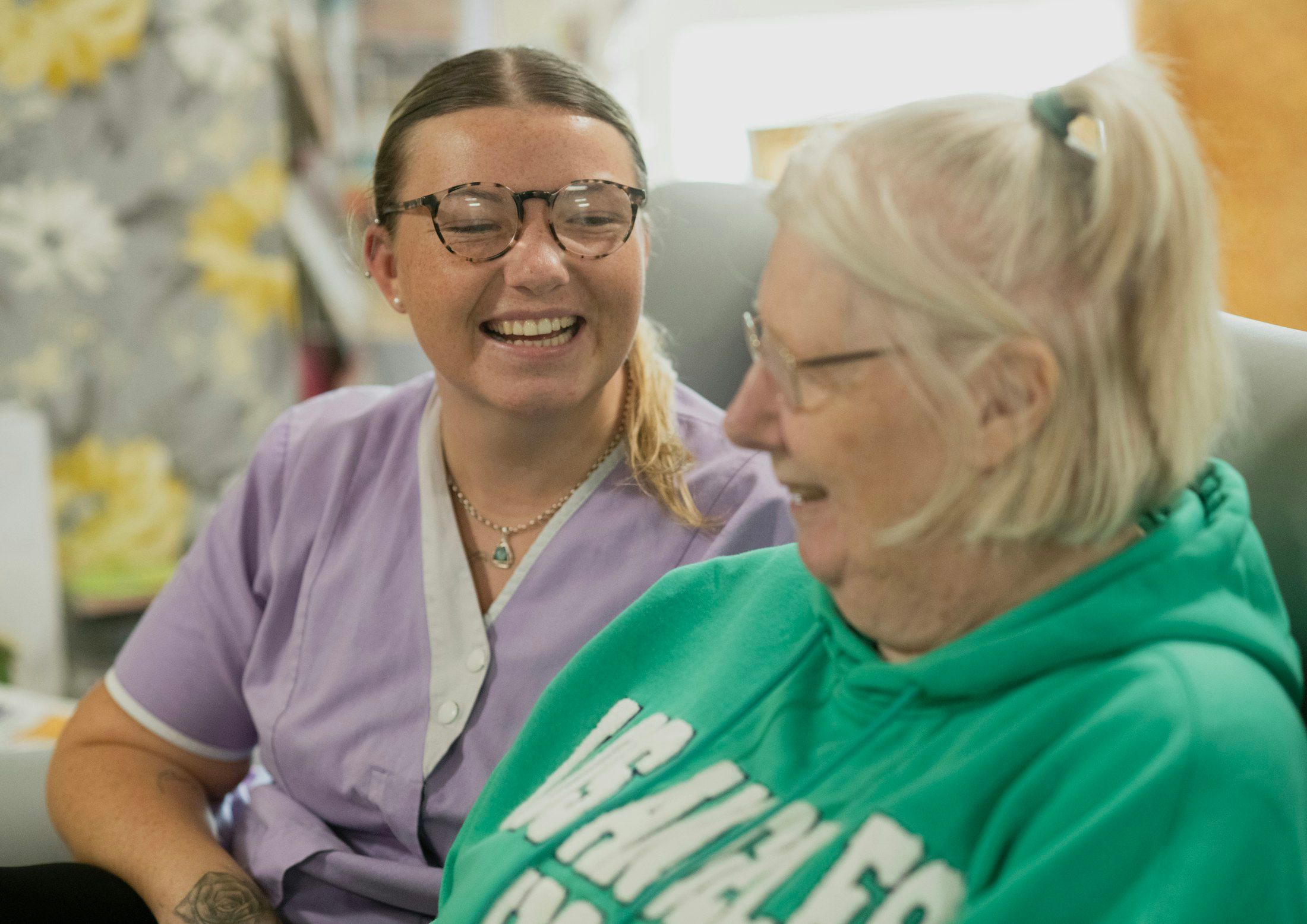 A carer and an older woman sharing a laugh in a sitting room.