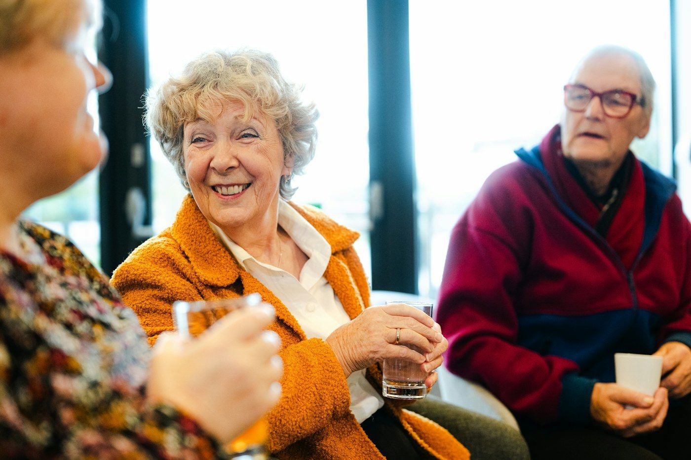 An older woman in an orange jacket laughing in a group of friends.