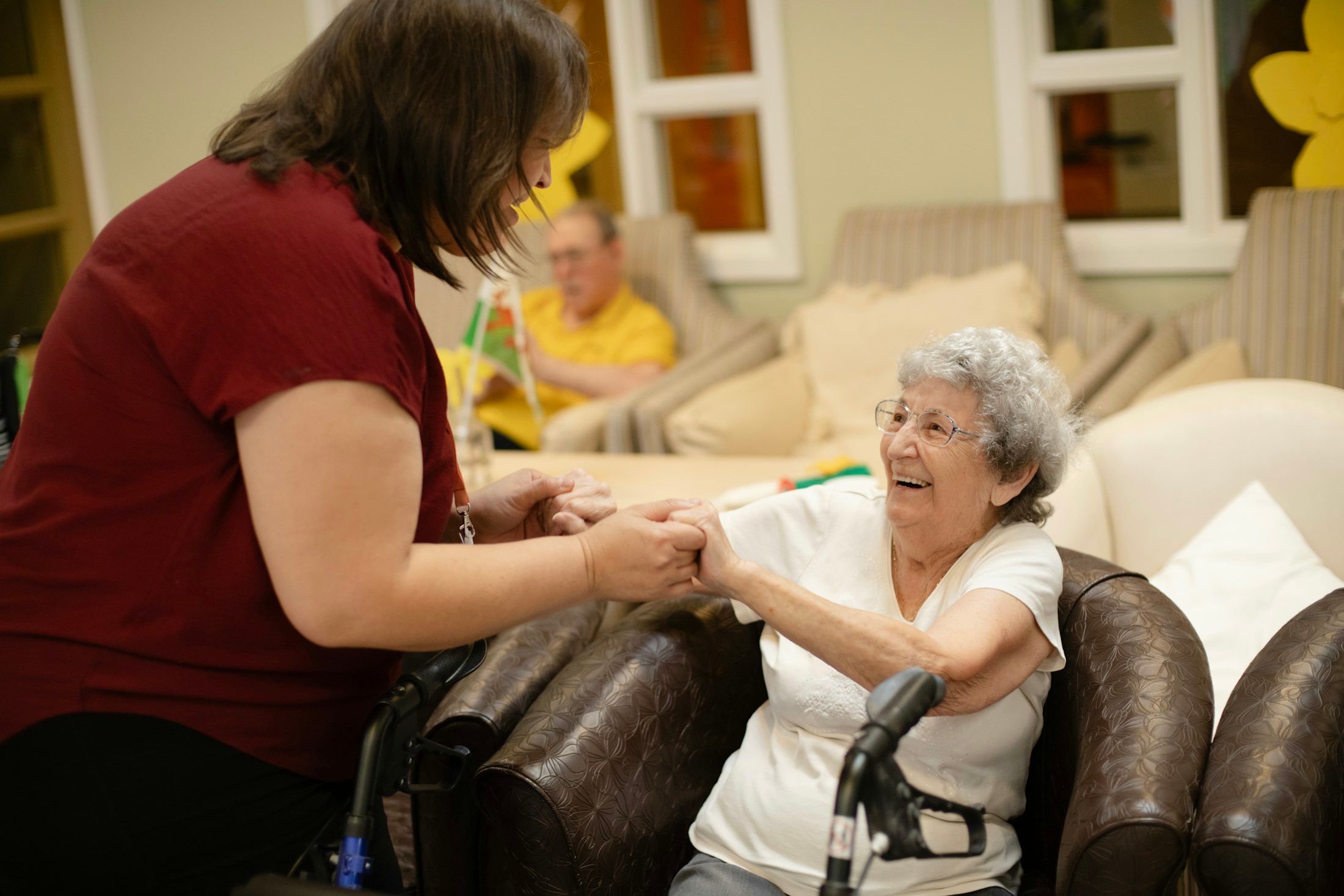 A carer holding an older woman’s hands in a lounge.