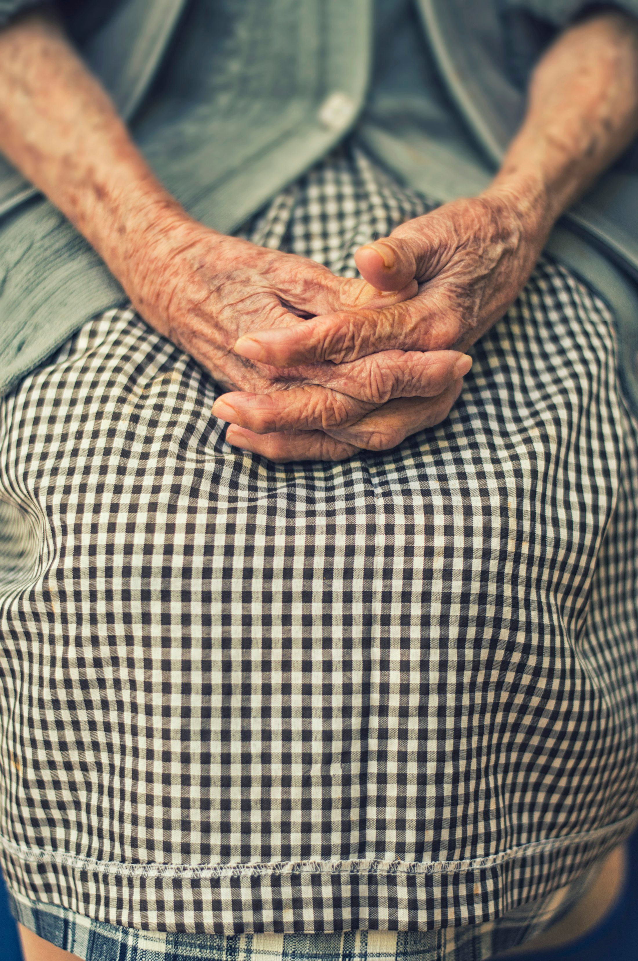 An older person’s hands resting together on a checked skirt.